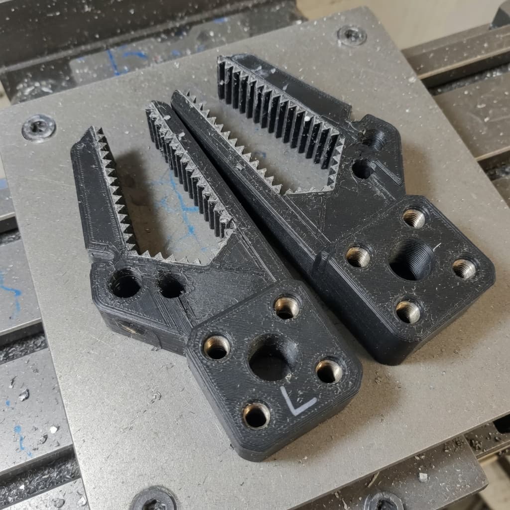 Pair of black printed gripper fingers with serrated jaws on a mill table.