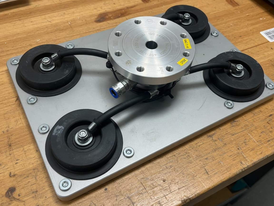Aluminum vacuum gripper plate with four suction cups on a wooden bench.